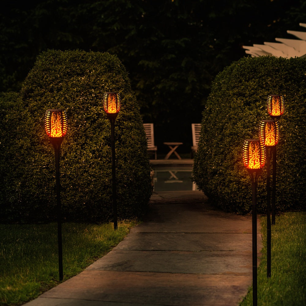 Facklor lyser på natten längs med väg i trädgård med fina flammor